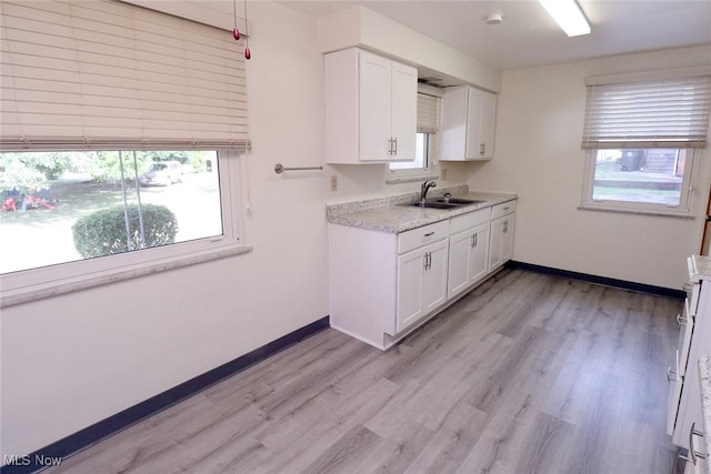 kitchen with range, sink, light wood-type flooring, light stone counters, and white cabinetry