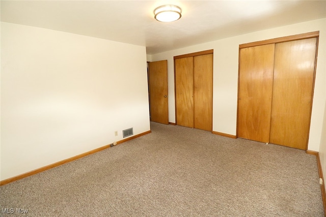 unfurnished bedroom featuring two closets and light colored carpet