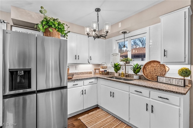 kitchen with stainless steel fridge, white cabinetry, and hanging light fixtures