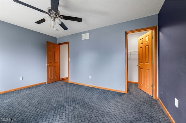 unfurnished bedroom featuring ceiling fan, a closet, a spacious closet, and dark carpet