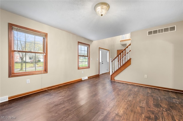 empty room featuring a textured ceiling, plenty of natural light, and dark wood-type flooring