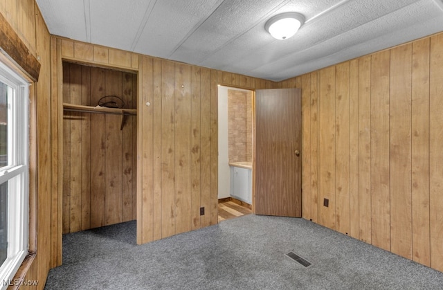 unfurnished bedroom featuring dark colored carpet, wood walls, a textured ceiling, and a closet