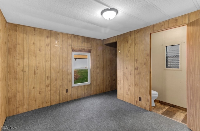 unfurnished bedroom featuring dark colored carpet, wood walls, a textured ceiling, and connected bathroom