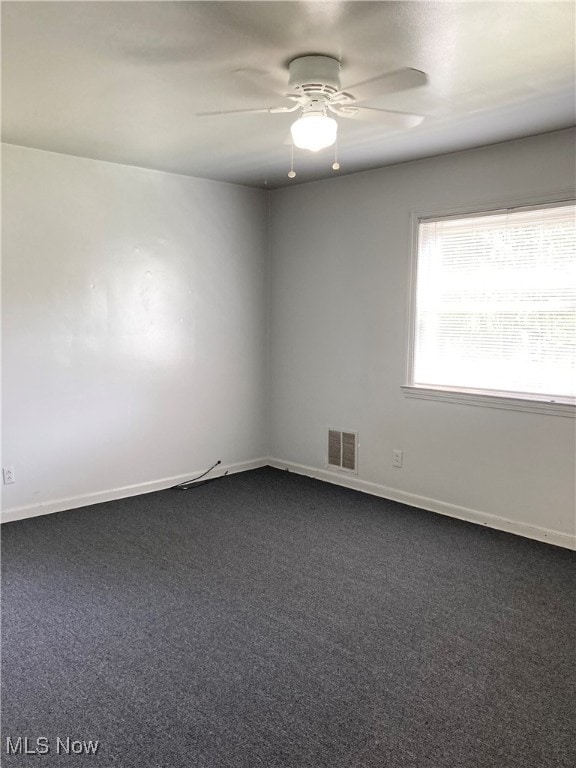 spare room featuring dark colored carpet and ceiling fan