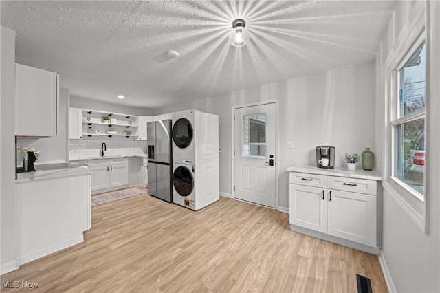 washroom featuring a textured ceiling, sink, light wood-type flooring, and stacked washer and dryer