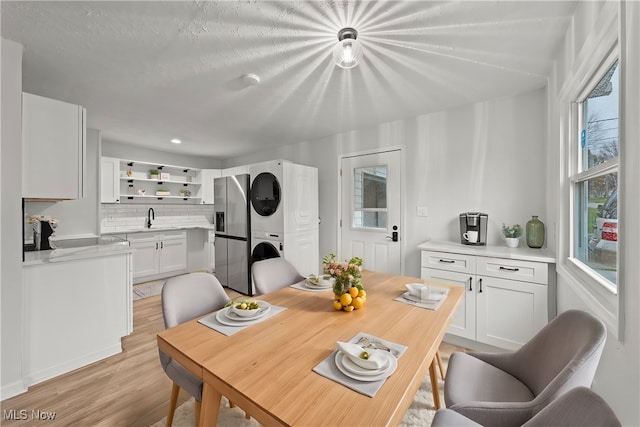 dining room with a textured ceiling, stacked washer / drying machine, light hardwood / wood-style floors, and sink