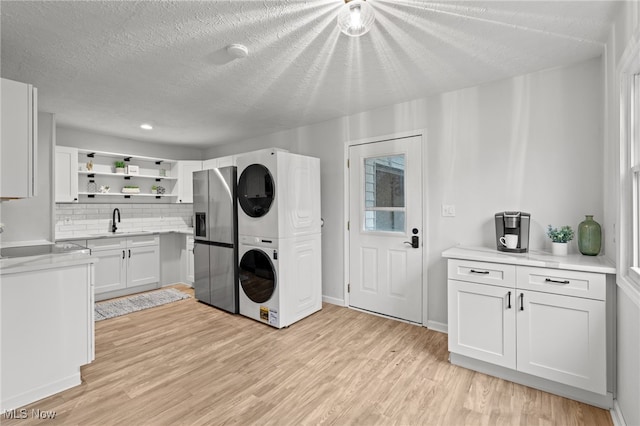 laundry area featuring stacked washer / dryer, sink, light hardwood / wood-style floors, and a textured ceiling