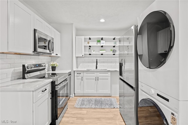 kitchen with sink, stainless steel appliances, light hardwood / wood-style flooring, stacked washer / dryer, and white cabinets