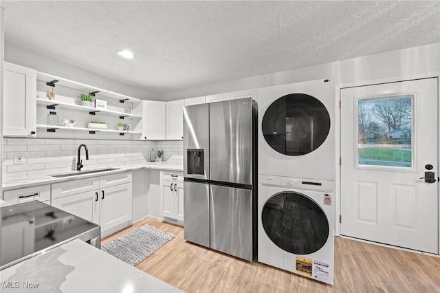 laundry area with a textured ceiling, stacked washer and dryer, light hardwood / wood-style floors, and sink