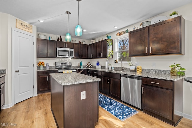 kitchen featuring appliances with stainless steel finishes, dark brown cabinetry, decorative light fixtures, a center island, and light hardwood / wood-style floors