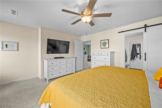 bedroom featuring ceiling fan, a barn door, light colored carpet, and a closet