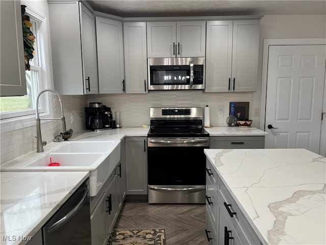 kitchen with gray cabinets, light stone countertops, sink, and appliances with stainless steel finishes