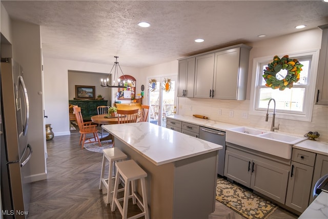 kitchen with stainless steel appliances, sink, a notable chandelier, a center island, and gray cabinets