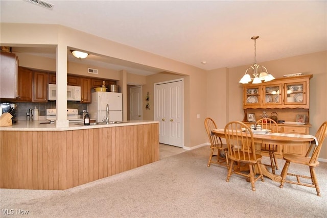 kitchen featuring white appliances, tasteful backsplash, light carpet, kitchen peninsula, and a chandelier