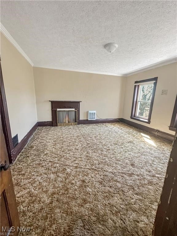 unfurnished living room with dark colored carpet, a textured ceiling, and ornamental molding