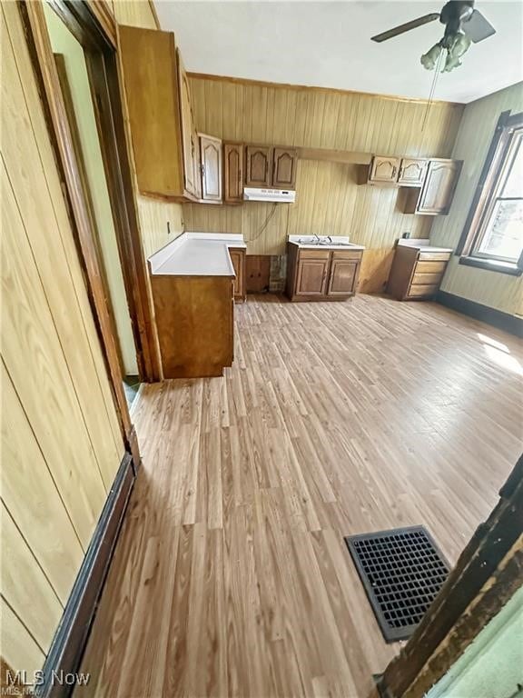 kitchen with ceiling fan, wood walls, and light wood-type flooring