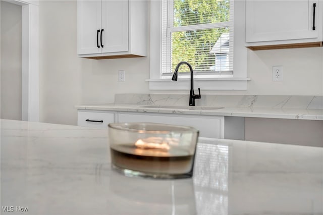 kitchen with white cabinets, light stone counters, and sink