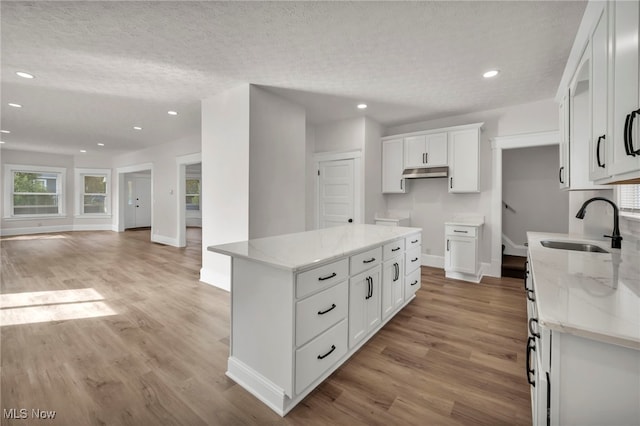 kitchen featuring a center island, sink, light stone countertops, light wood-type flooring, and white cabinetry