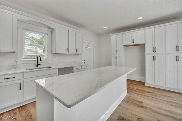 kitchen featuring white cabinetry, sink, a center island, and light wood-type flooring