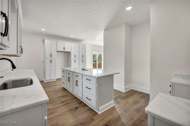 kitchen featuring a center island, light stone countertops, white cabinetry, and sink