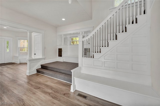 staircase featuring wood-type flooring and decorative columns