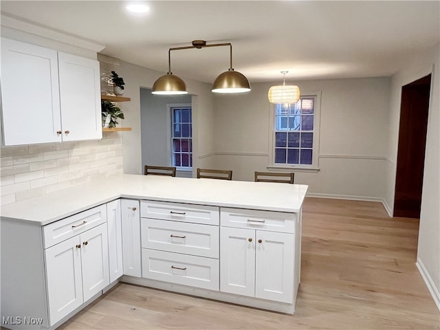 kitchen with pendant lighting, white cabinetry, kitchen peninsula, and light hardwood / wood-style flooring