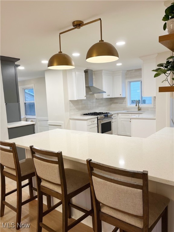 kitchen with sink, white cabinets, wall chimney range hood, and stainless steel gas range