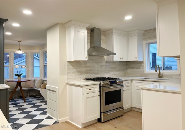 kitchen with gas stove, white cabinetry, sink, and wall chimney range hood