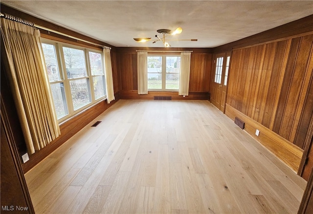 spare room featuring wooden walls, a healthy amount of sunlight, and light wood-type flooring