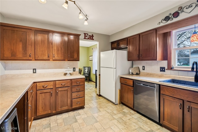 kitchen featuring track lighting, white refrigerator, sink, stainless steel dishwasher, and decorative backsplash