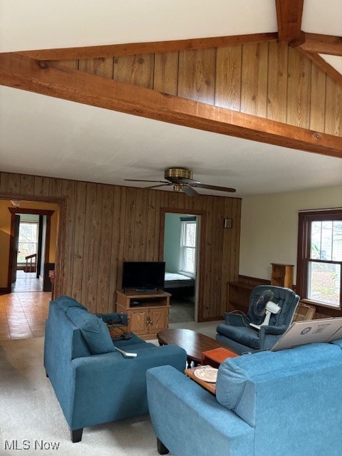 living room featuring beamed ceiling, plenty of natural light, wooden walls, and ceiling fan