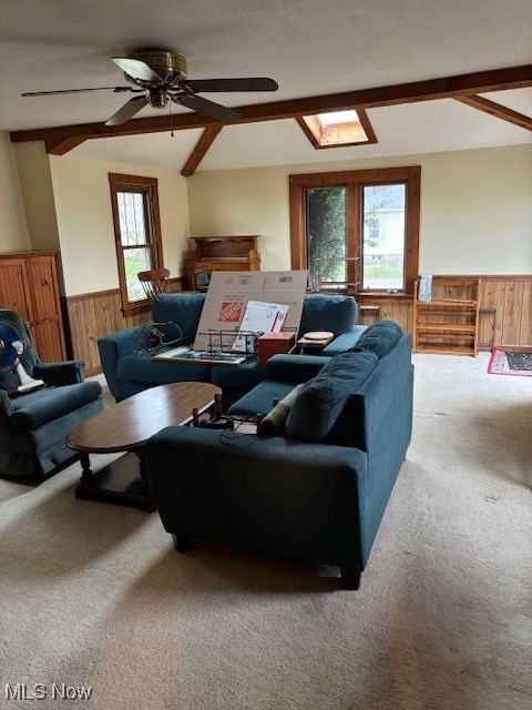 carpeted living room featuring ceiling fan, a healthy amount of sunlight, wooden walls, and a skylight