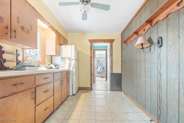 kitchen with light tile patterned flooring, ceiling fan, white refrigerator, and wooden walls