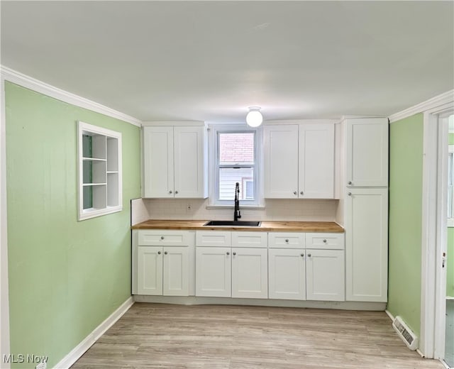 kitchen with white cabinets, backsplash, butcher block countertops, and sink