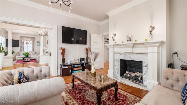 living room featuring a premium fireplace, an inviting chandelier, ornamental molding, and light wood-type flooring