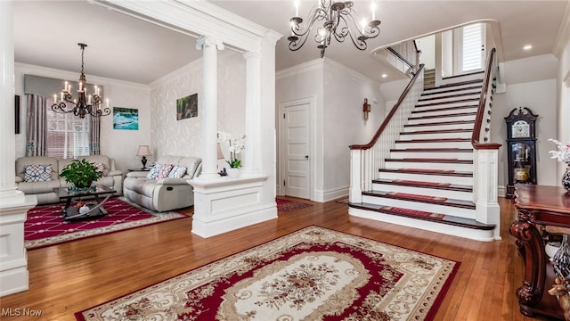 entrance foyer featuring ornamental molding, hardwood / wood-style flooring, decorative columns, and a notable chandelier