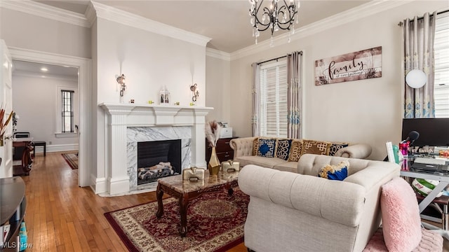 living room featuring crown molding, a high end fireplace, a notable chandelier, and light wood-type flooring