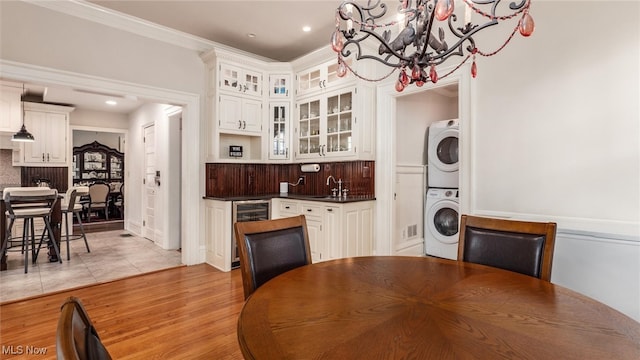 kitchen with white cabinets, light hardwood / wood-style flooring, stacked washer / drying machine, and sink