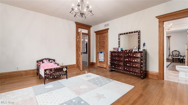 bedroom featuring connected bathroom, wood-type flooring, and a notable chandelier