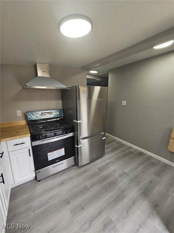 kitchen featuring wall chimney exhaust hood, light hardwood / wood-style flooring, butcher block countertops, white cabinets, and appliances with stainless steel finishes