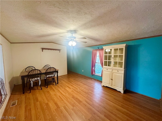 dining room with ceiling fan, crown molding, lofted ceiling, a textured ceiling, and light wood-type flooring