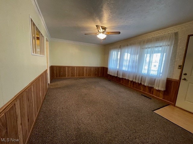 carpeted spare room with ceiling fan, wood walls, and a textured ceiling