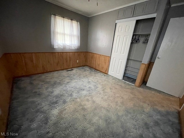 unfurnished bedroom with ornamental molding, carpet floors, a closet, and wooden walls