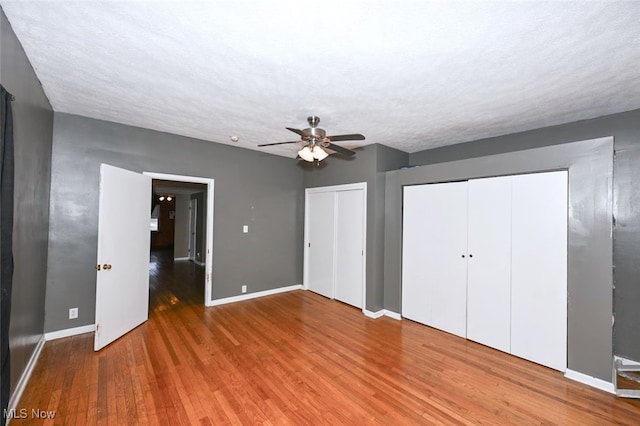 unfurnished bedroom with wood-type flooring, a textured ceiling, ceiling fan, and multiple closets