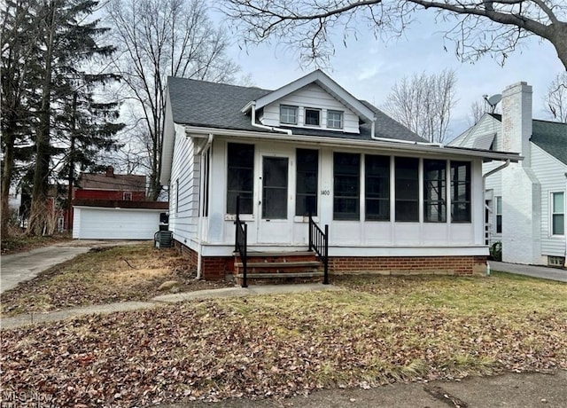 bungalow-style home with an outbuilding, a front yard, a garage, and a sunroom