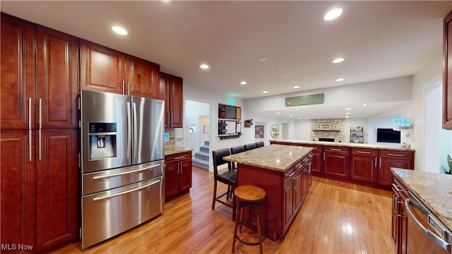 kitchen featuring a center island, a kitchen breakfast bar, light stone countertops, light hardwood / wood-style floors, and stainless steel appliances