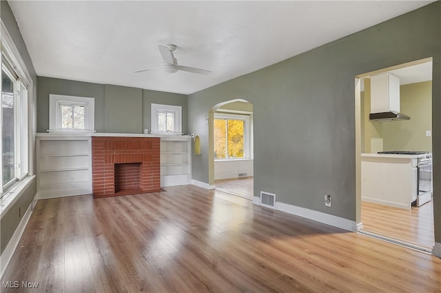 unfurnished living room with a fireplace, light wood-type flooring, and ceiling fan