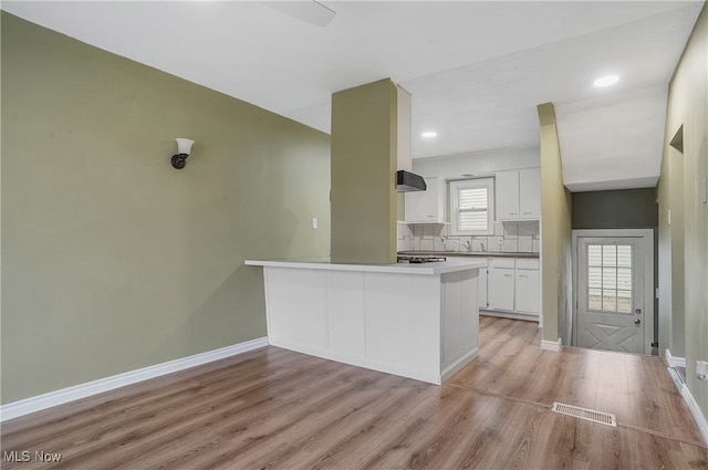 kitchen with decorative backsplash, white cabinetry, kitchen peninsula, and light hardwood / wood-style flooring