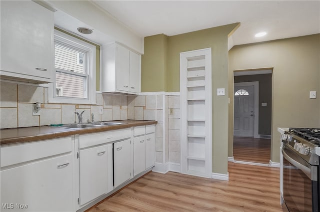 kitchen featuring decorative backsplash, sink, light hardwood / wood-style flooring, stainless steel range oven, and white cabinetry