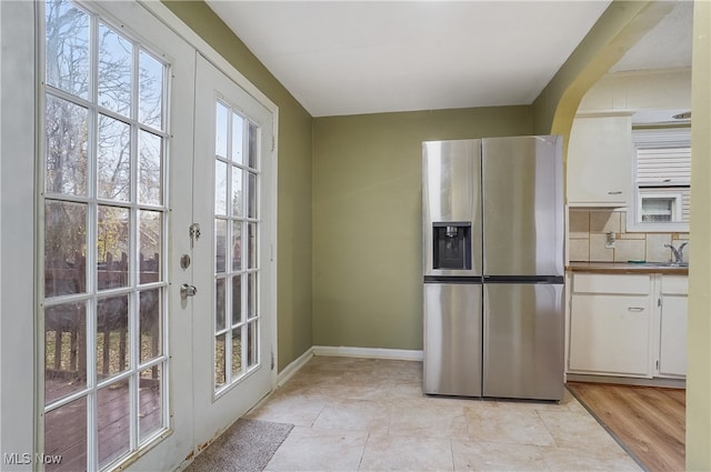 kitchen featuring stainless steel refrigerator with ice dispenser, backsplash, white cabinetry, and french doors